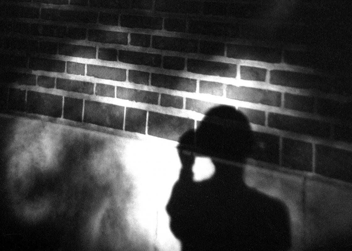 student walking at night with shadow on brick wall
